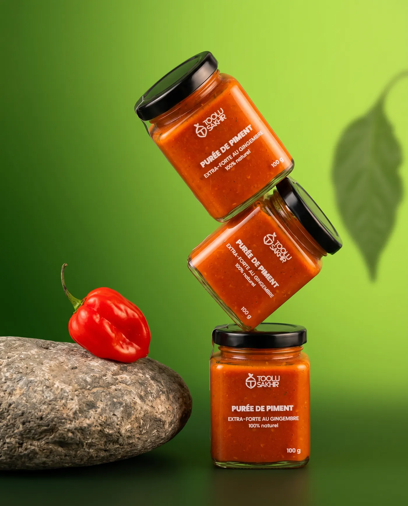 Bocaux de purée de piment en lévitation sur fond vert, un piment rouge posé sur une pierre