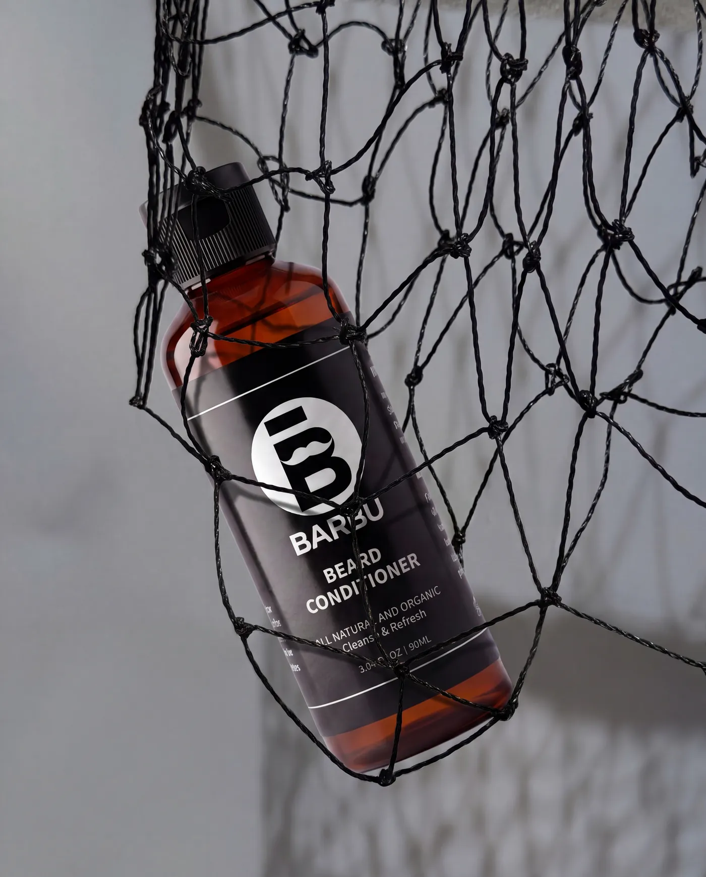 Flacon Barbu Beard Wash suspendu dans un filet, sur fond gris