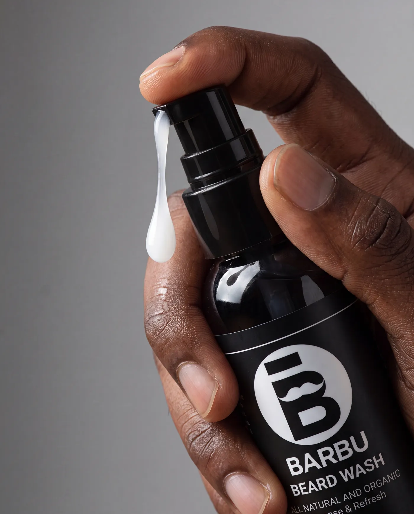 Main tenant un flacon Barbu Beard Wash sur fond gris