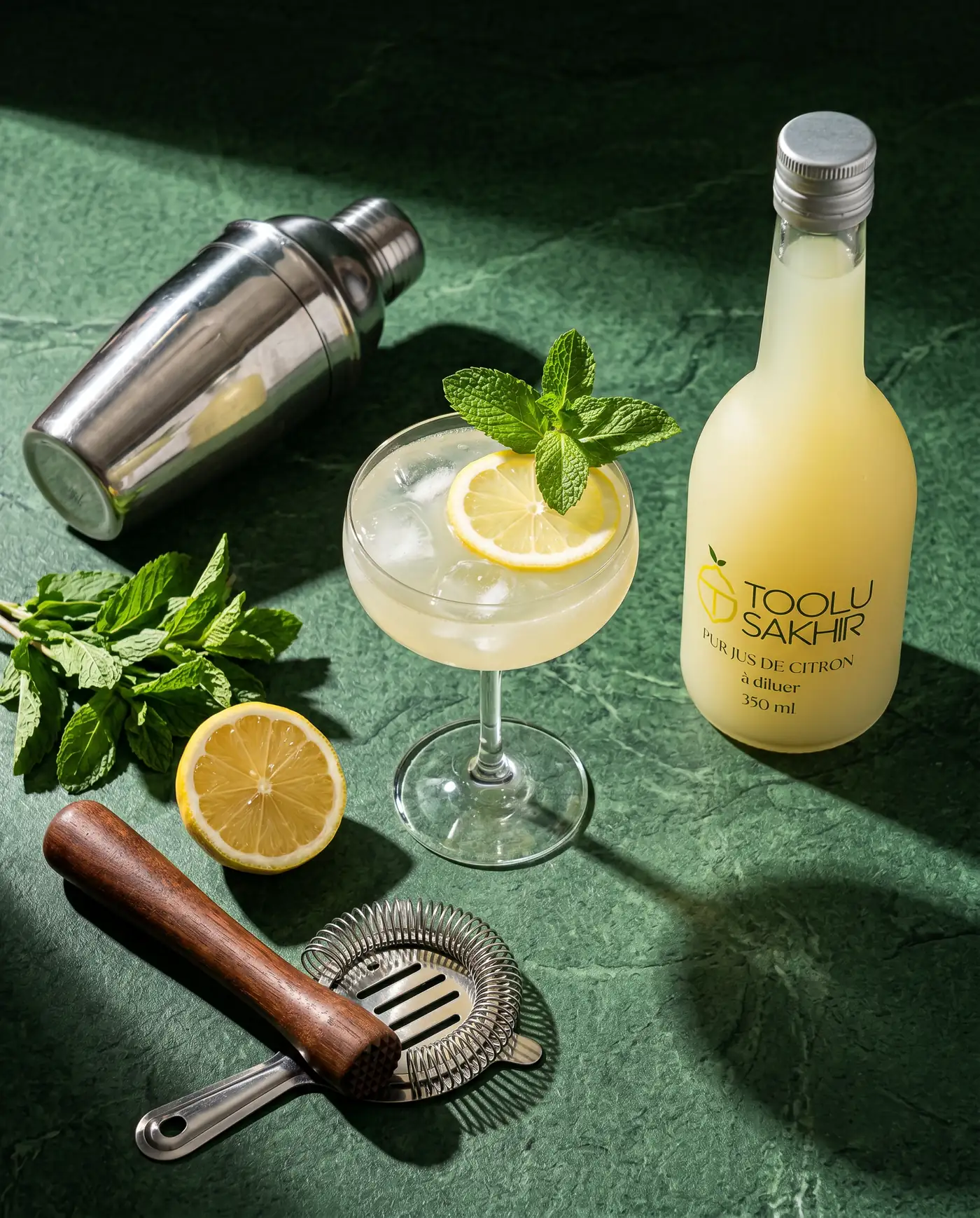 Bouteille Toolu Sakhir, cocktail dans un verre et shaker, sur fond vert